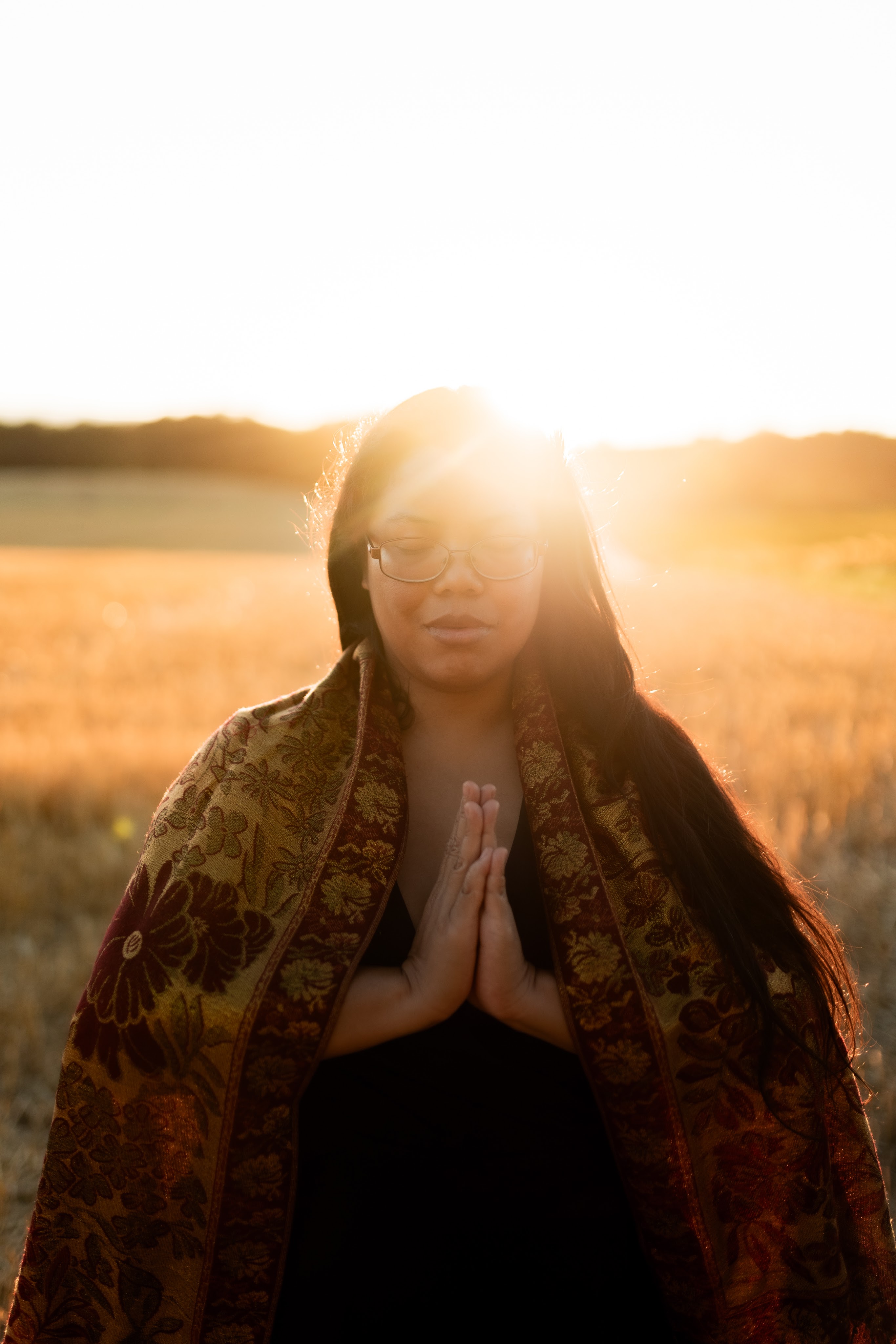 portrait d'une thérapeute en constellations familiales et systémiques et thérapie psycho-spirituelle en position de prière, les yeux fermés, dans un champ de blé situé vers Morges, Renens et Lausanne, dans le canton de Vaud en Suisse