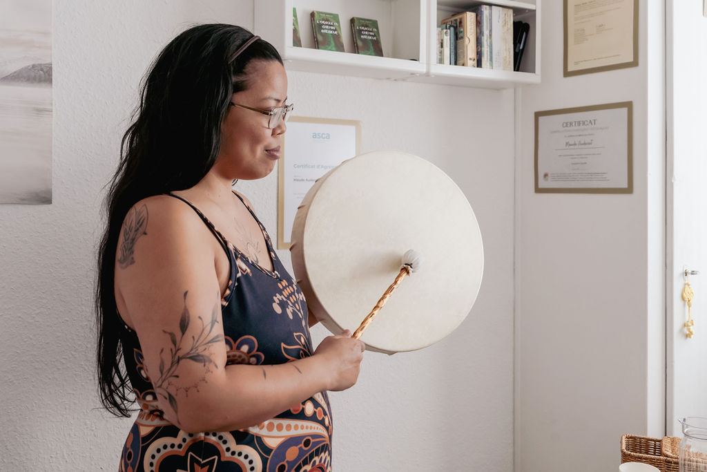portrait d'une thérapeute holistique en Suisse tenant un tambour chamanique, lors d'une séance de constellations familiales et systémiques près de Lausanne (Vaud) et Renens, à Morges